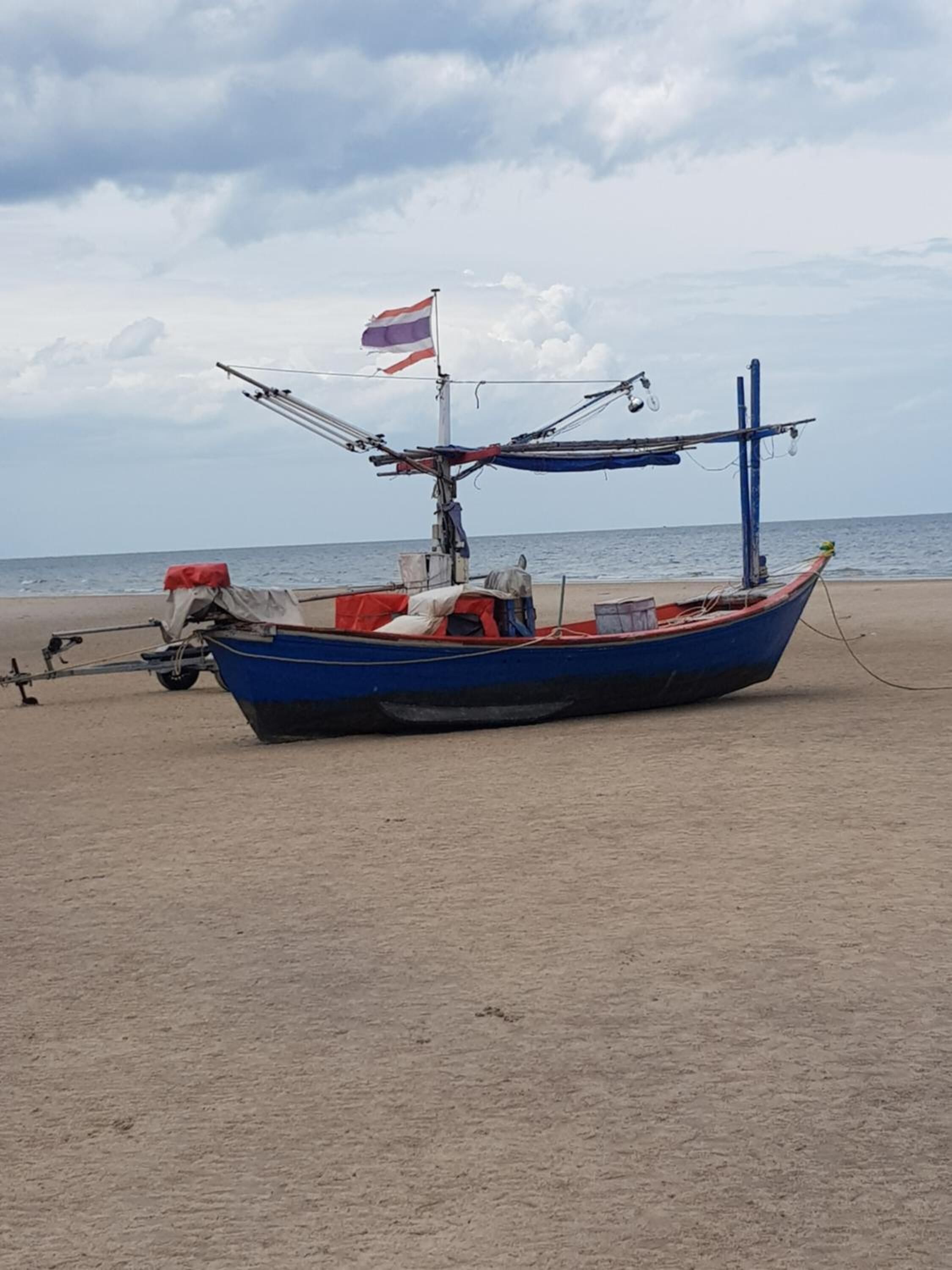 A blue boat with a flag on a sandy beach.
