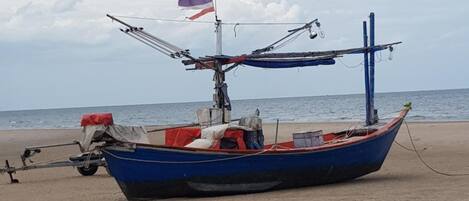 A blue boat with a flag on a sandy beach.