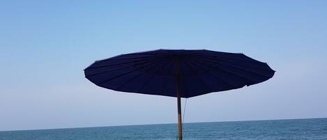 Dos sillas de playa con cojines amarillos y una sombrilla azul oscuro sobre arena, con el océano al fondo.