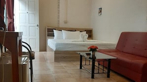 A hotel room with a bed, a red sofa, a small table with a vase, an air conditioning unit, and a door. - Plaza Hua Hin (Hua Hin)