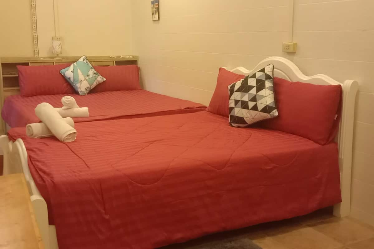 Ein Schlafzimmer mit roter Bettdecke, zwei Kissen, einem Nachttisch aus Holz und einem kleinen Tisch mit Tassen.