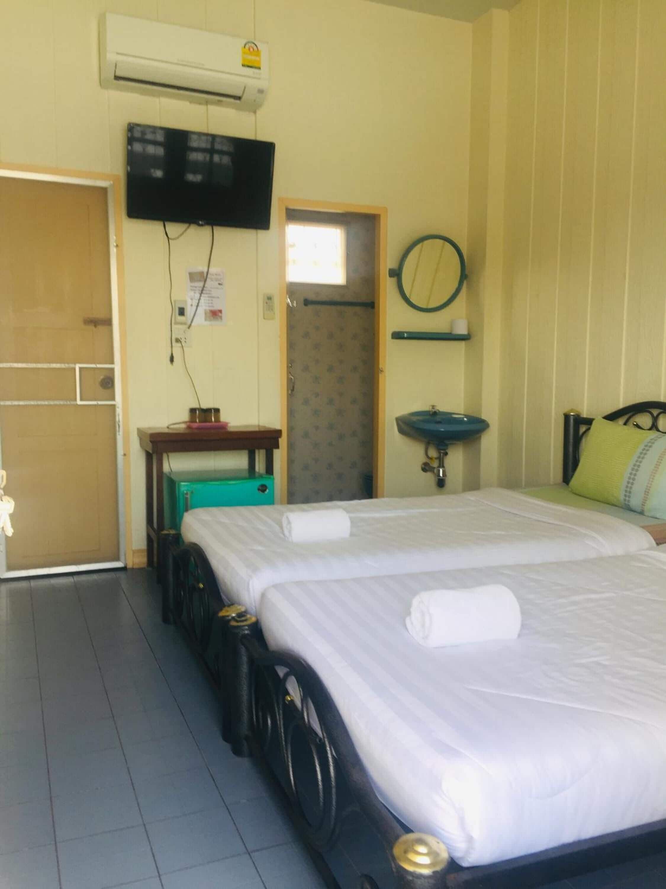 Habitación de hotel con dos camas, un televisor montado en la pared, un escritorio pequeño con una silla, un espejo redondo y una ventana.