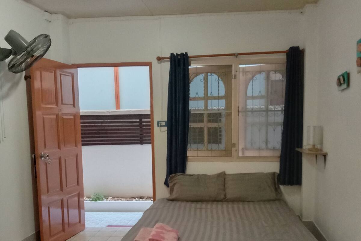 Ein Schlafzimmer mit einem Bett, einem Ventilator, einem Fenster mit Vorhängen und einer Tür.