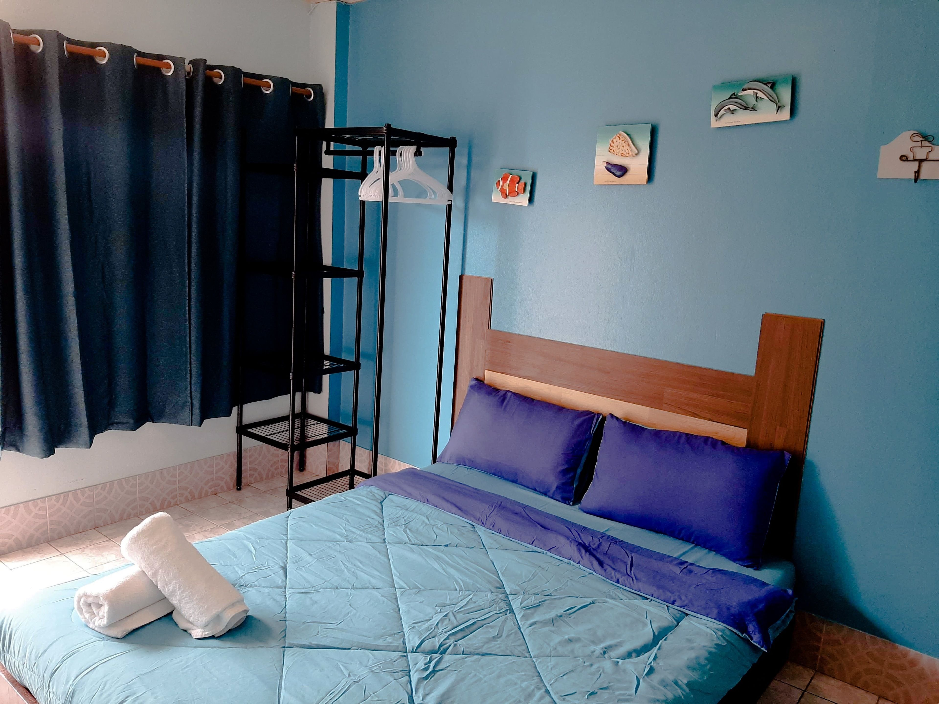A bedroom with a bed, a wooden headboard, a blue wall, a black metal rack, and a curtain.