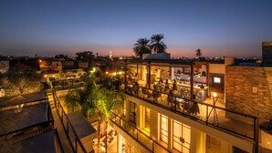 Un restaurante en la azotea con mesas al aire libre, palmeras y vistas del horizonte de la ciudad al atardecer.