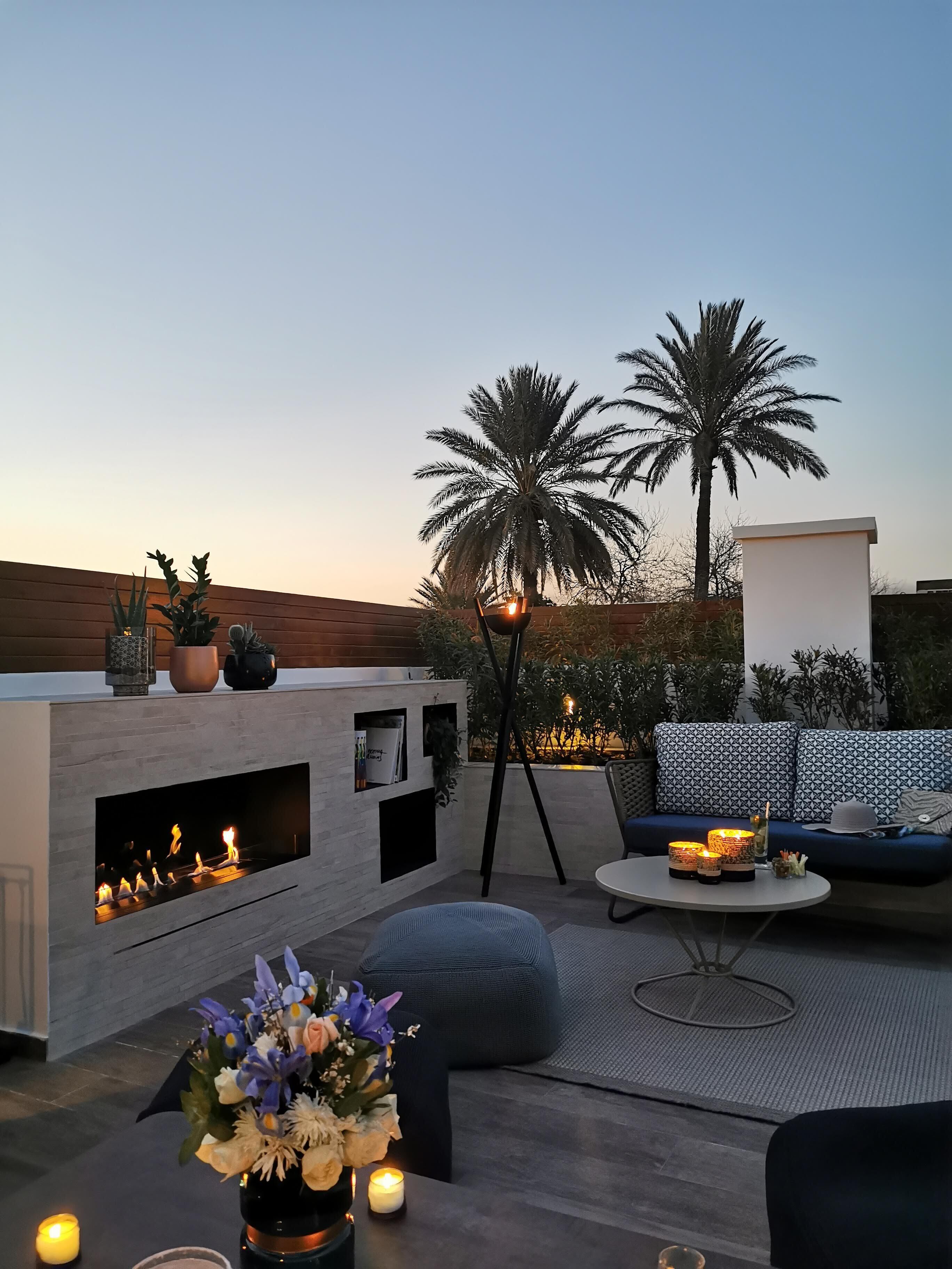 An outdoor lounge area with a built-in fireplace, seating, and decorative plants.