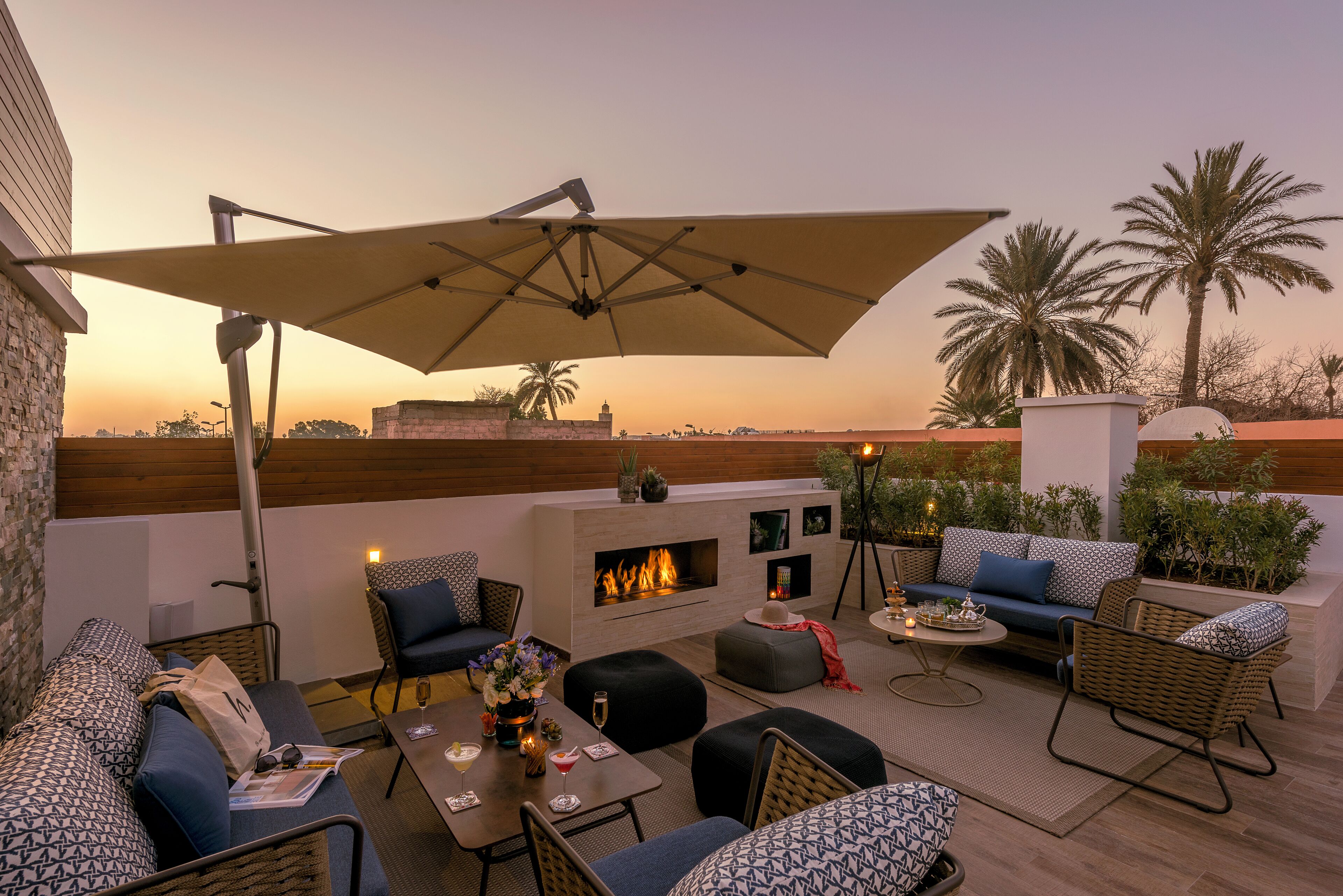 Eine Dachterrasse mit Sitzgelegenheiten im Freien, einer Feuerstelle und Blick auf Palmen.