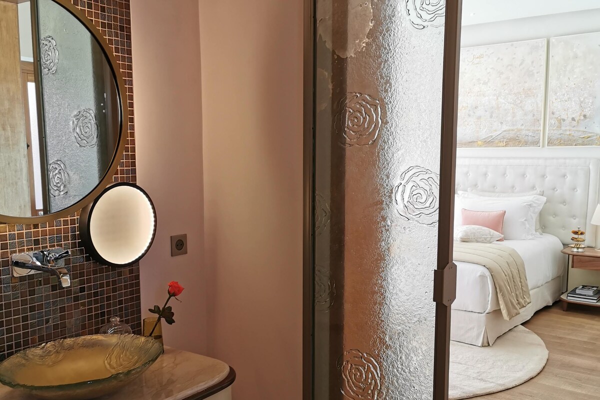 A bathroom with a glass sink, a round mirror, and a rose decoration.
