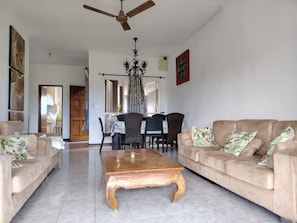 A spacious living room with a ceiling fan, a wooden coffee table, and two sofas with floral cushions. - Three Bedroom Apartment by Dakz (Trou aux Biches)