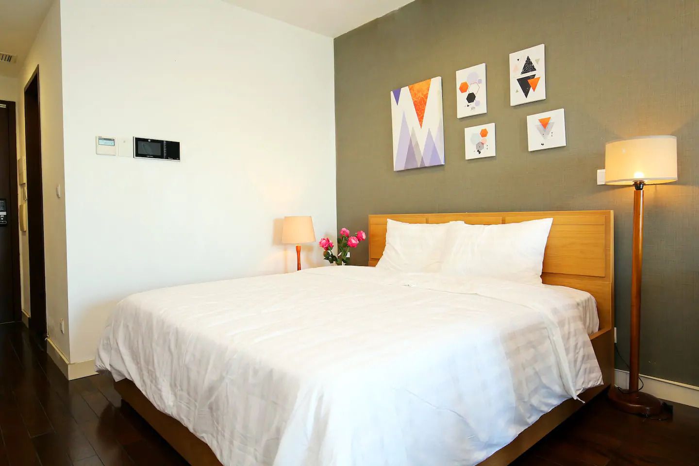 Habitación de hotel con una cama grande, dos lámparas de noche, un jarrón con flores y arte abstracto en la pared.