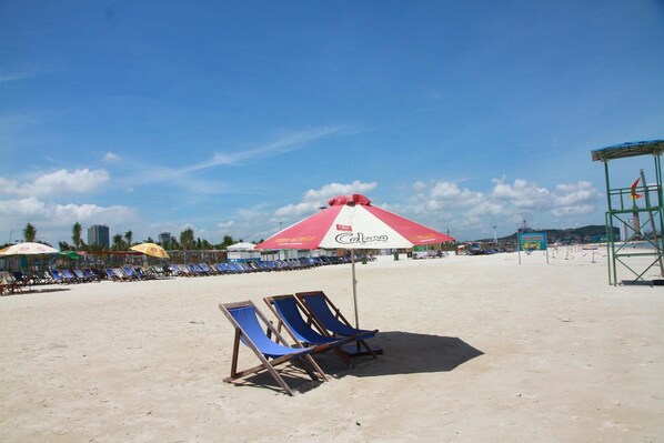 A beach with rows of blue lounge chairs and a red and white umbrella. - The Marine Hotel (Bai Chay)