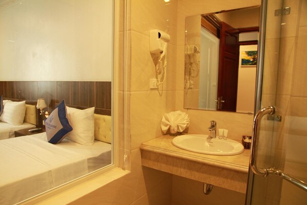 A hotel room with a bed, a bathroom with a sink and mirror, and a shower area. - The Marine Hotel (Bai Chay)