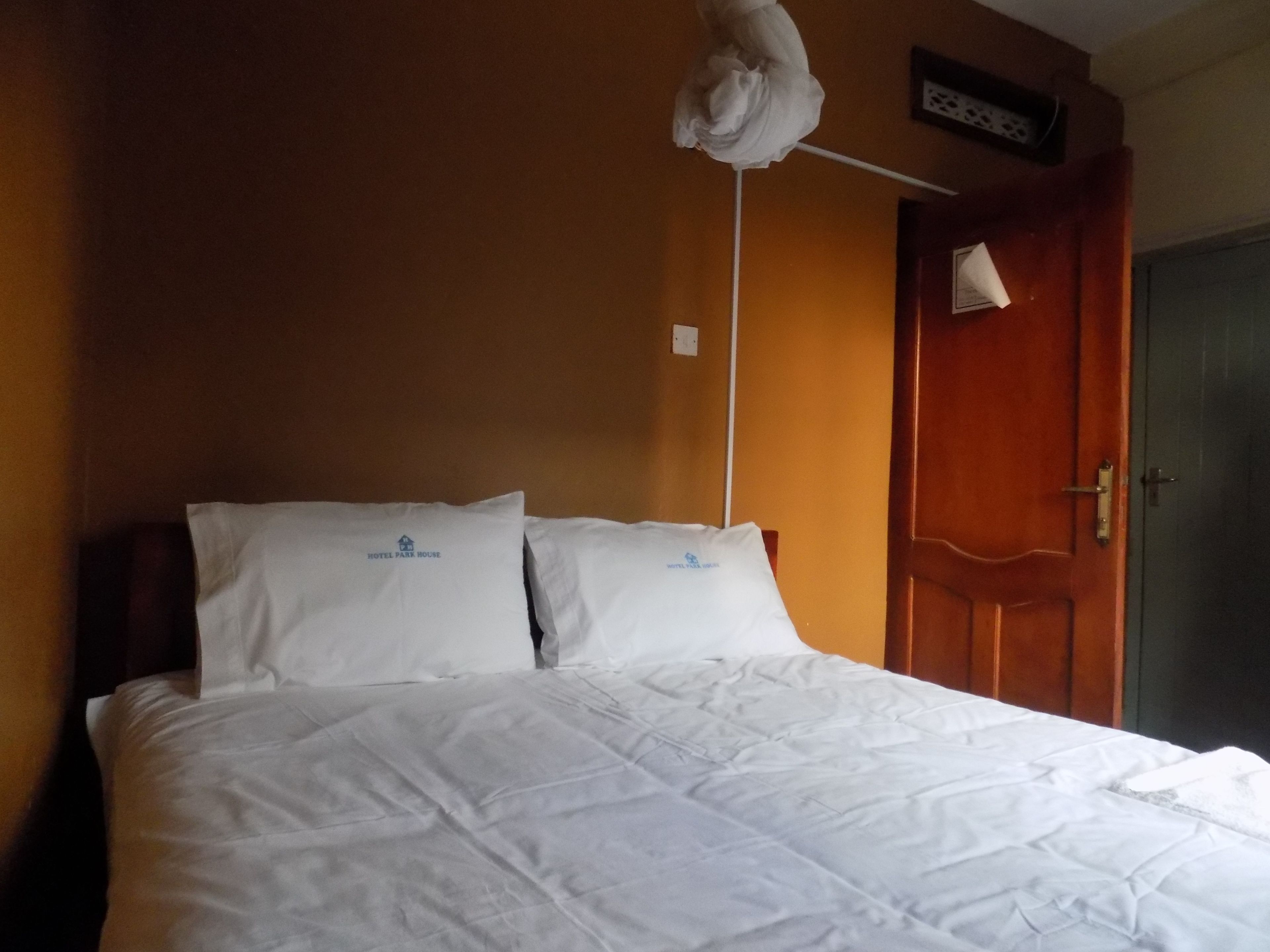 Een hotelkamer met een bed, kussens, een houten deur en een wandlamp.