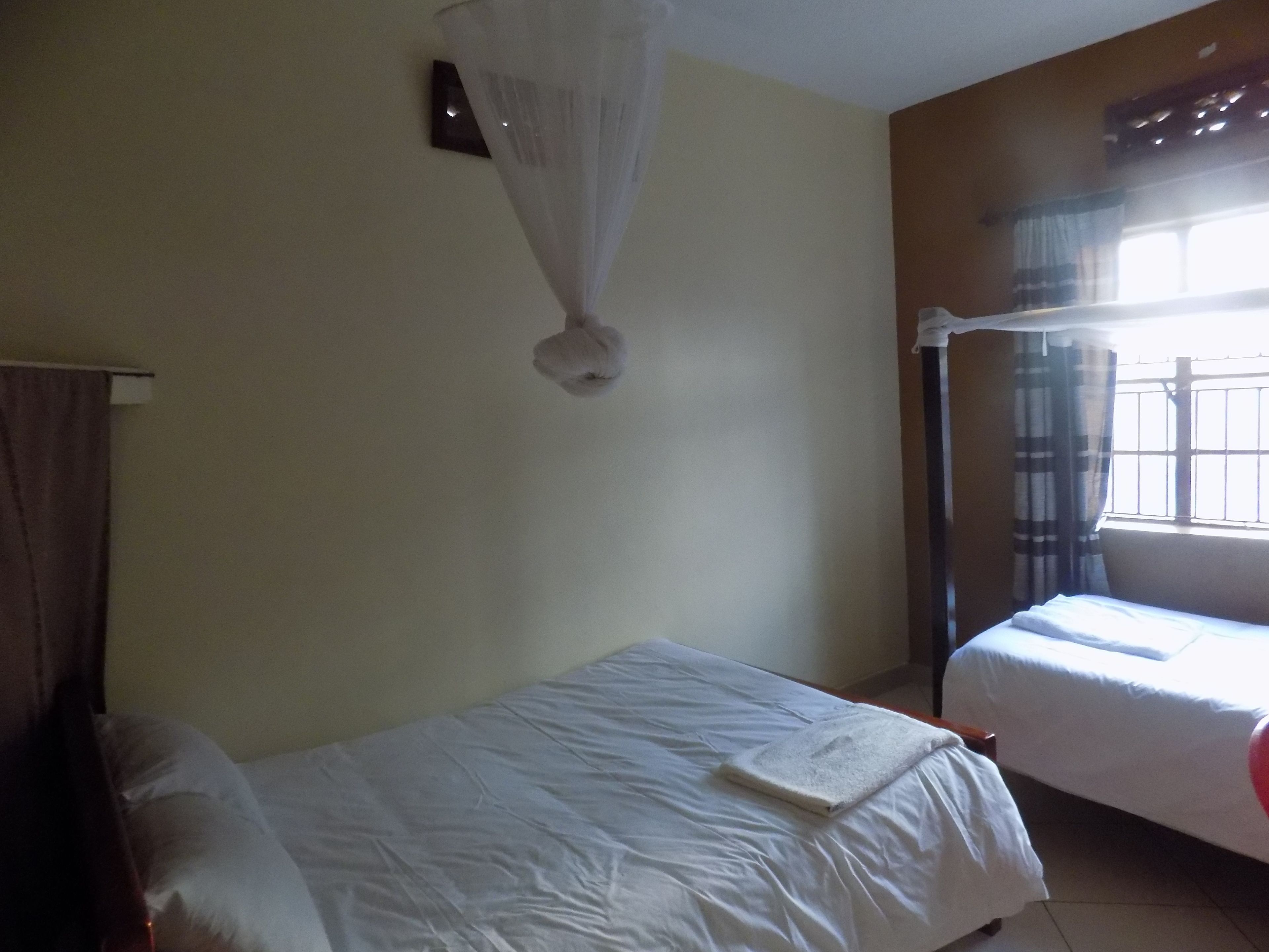 Een kamer met twee bedden, een klamboe, een raam met gordijnen en een wandlamp.