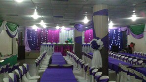 A banquet hall with rows of white chairs and purple tablecloths, a central aisle, and draped fabric on the walls. - Eastern Comfort and Suites (Umuahia)
