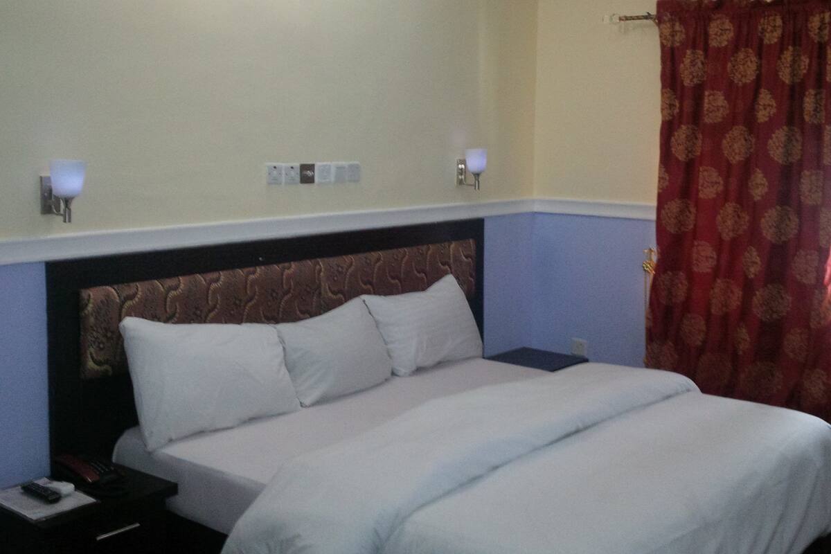A hotel room with a bed, bedside tables, a nightstand, a lamp, and a curtain.