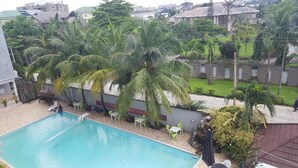 A swimming pool surrounded by palm trees and a garden. - Eastern Comfort and Suites (Umuahia)