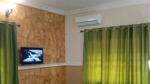 A hotel room with a wooden accent wall, a mounted TV, green curtains, and a bed with white bedding. - Eastern Comfort and Suites (Umuahia)