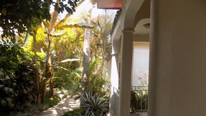 A covered walkway with potted plants, a stone path, and a view of a building in the background. - Cielo Country Inn (Ishaka)