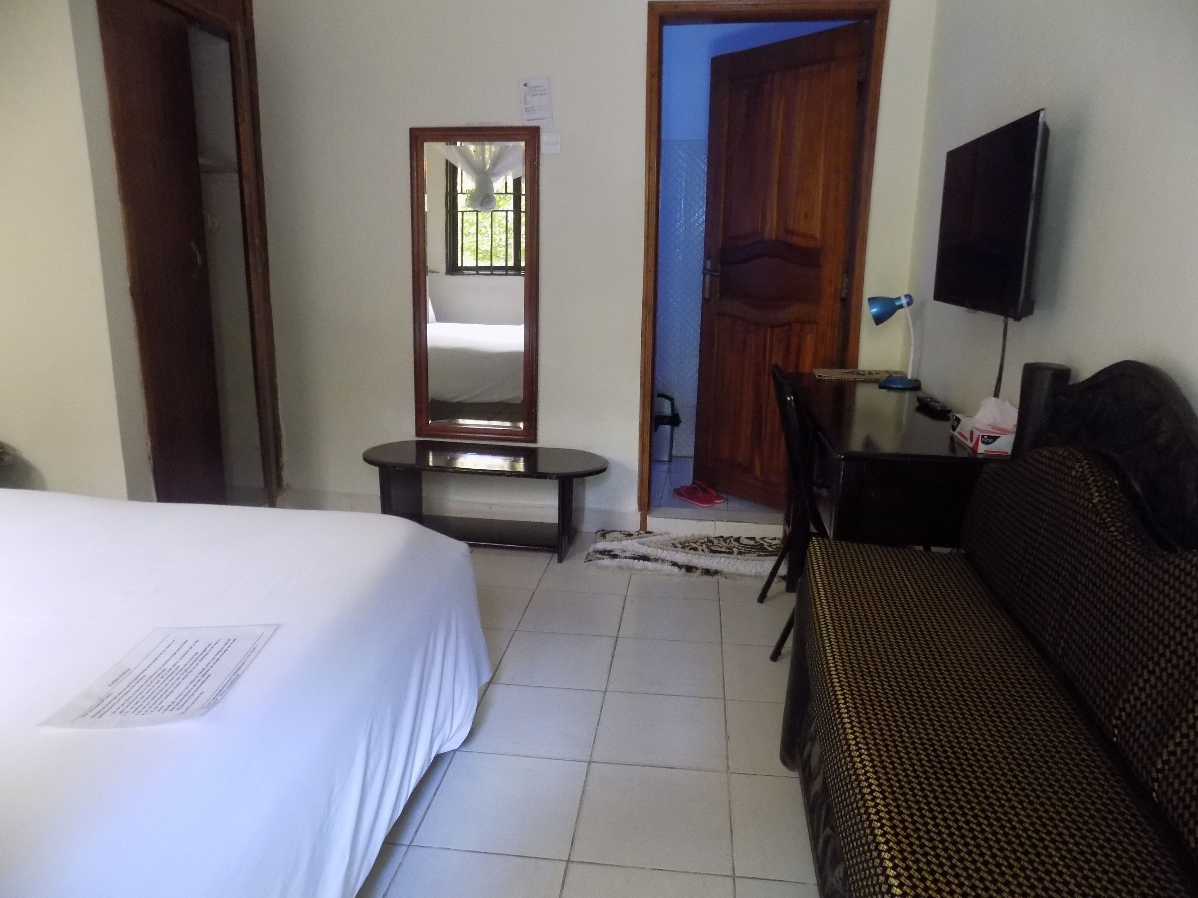 Una habitación de hotel con cama, sofá, televisión, espejo y una pequeña mesa.