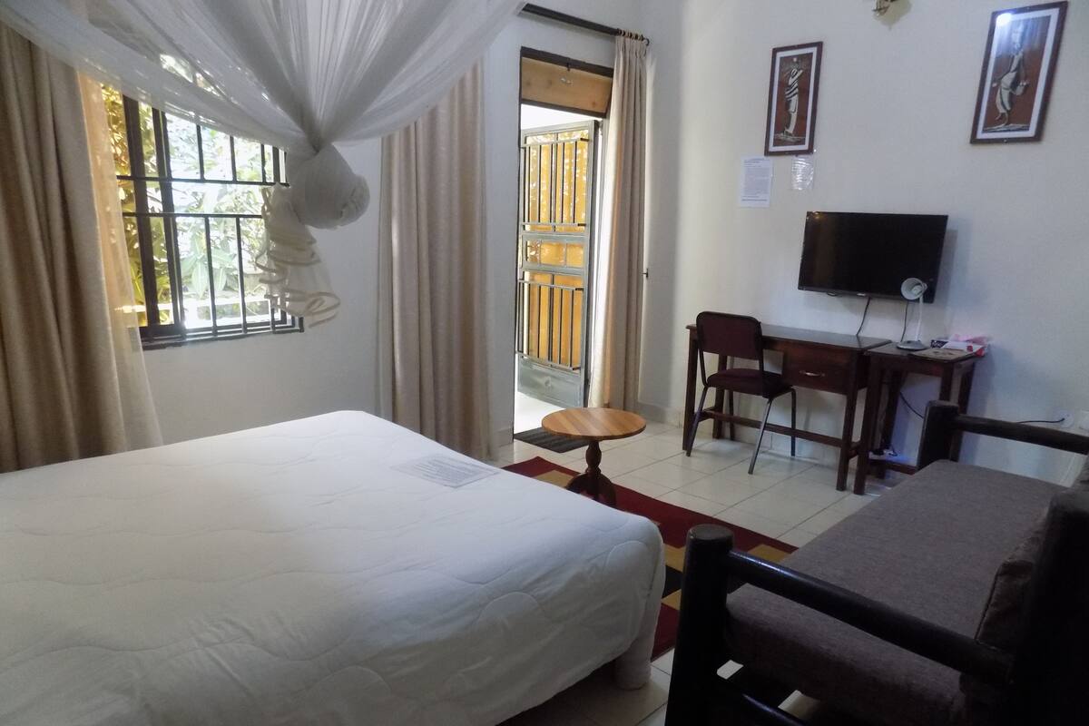 Quarto de hotel com cama, escrivaninha, cadeira, televisão e janela com cortinas.