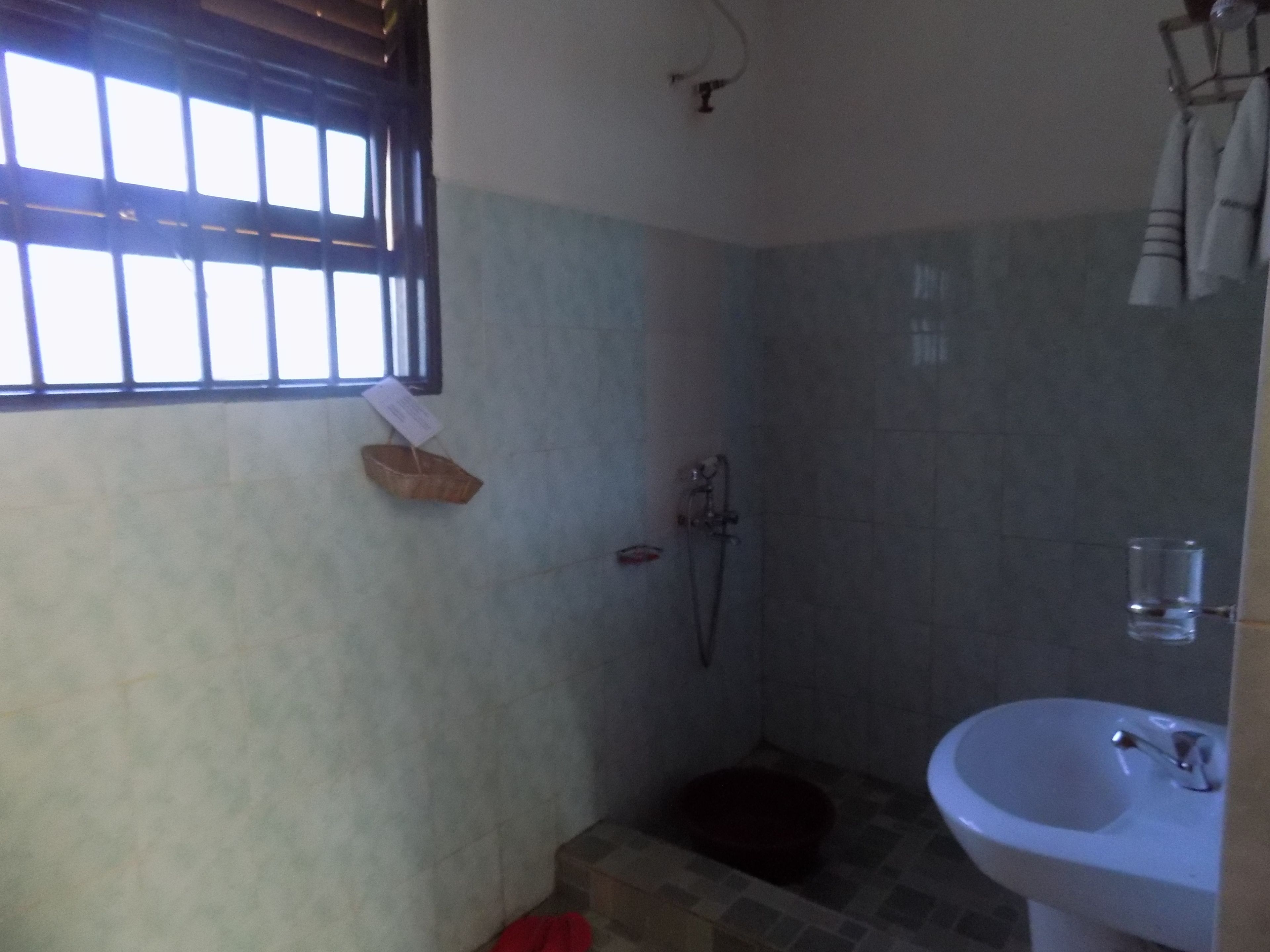 Un baño pequeño con ducha, lavamanos y ventana con persianas.