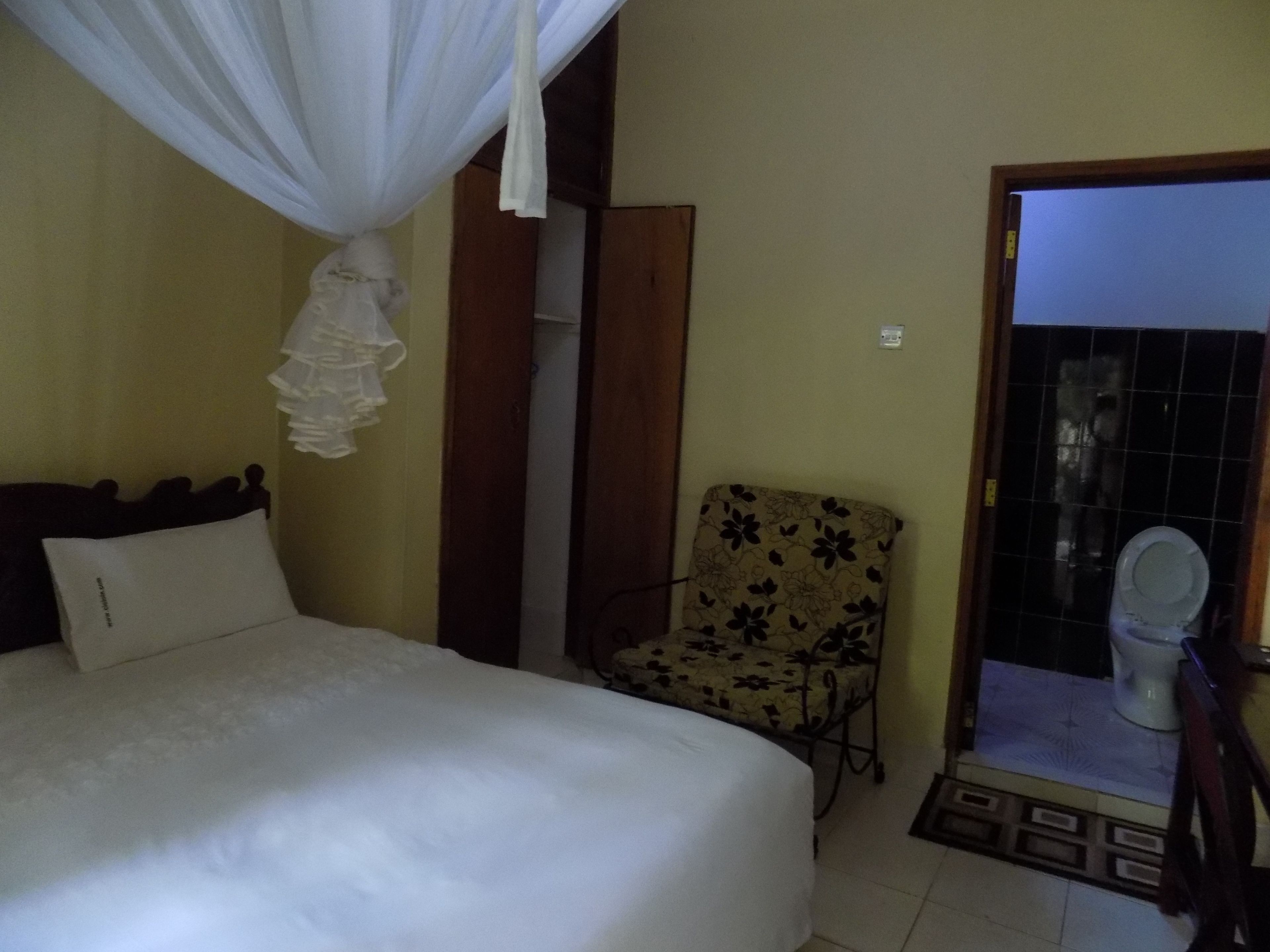 A bedroom with a bed, a chair, a curtain, and a view of a bathroom.