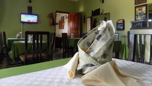 A dining area with green walls, a television mounted on the wall, and a table with a checkered tablecloth. - Cielo Country Inn (Ishaka)