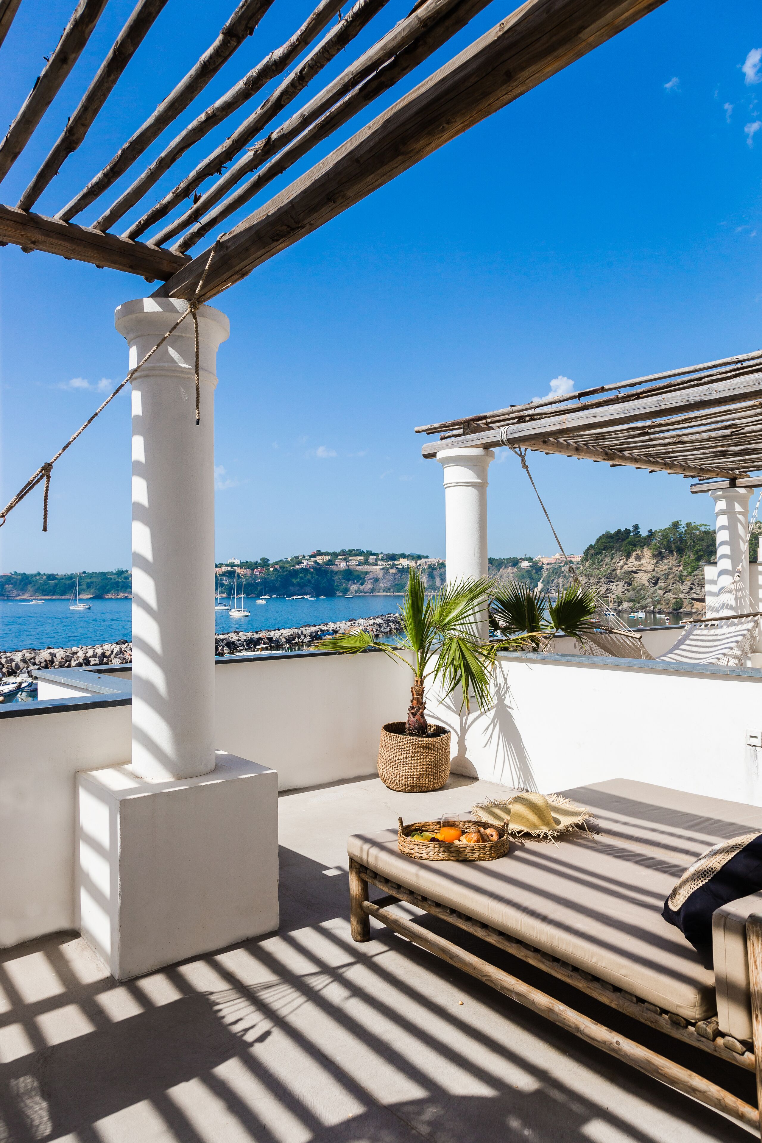 A terrace with a white column, a wooden bench, a woven basket, and a potted plant.