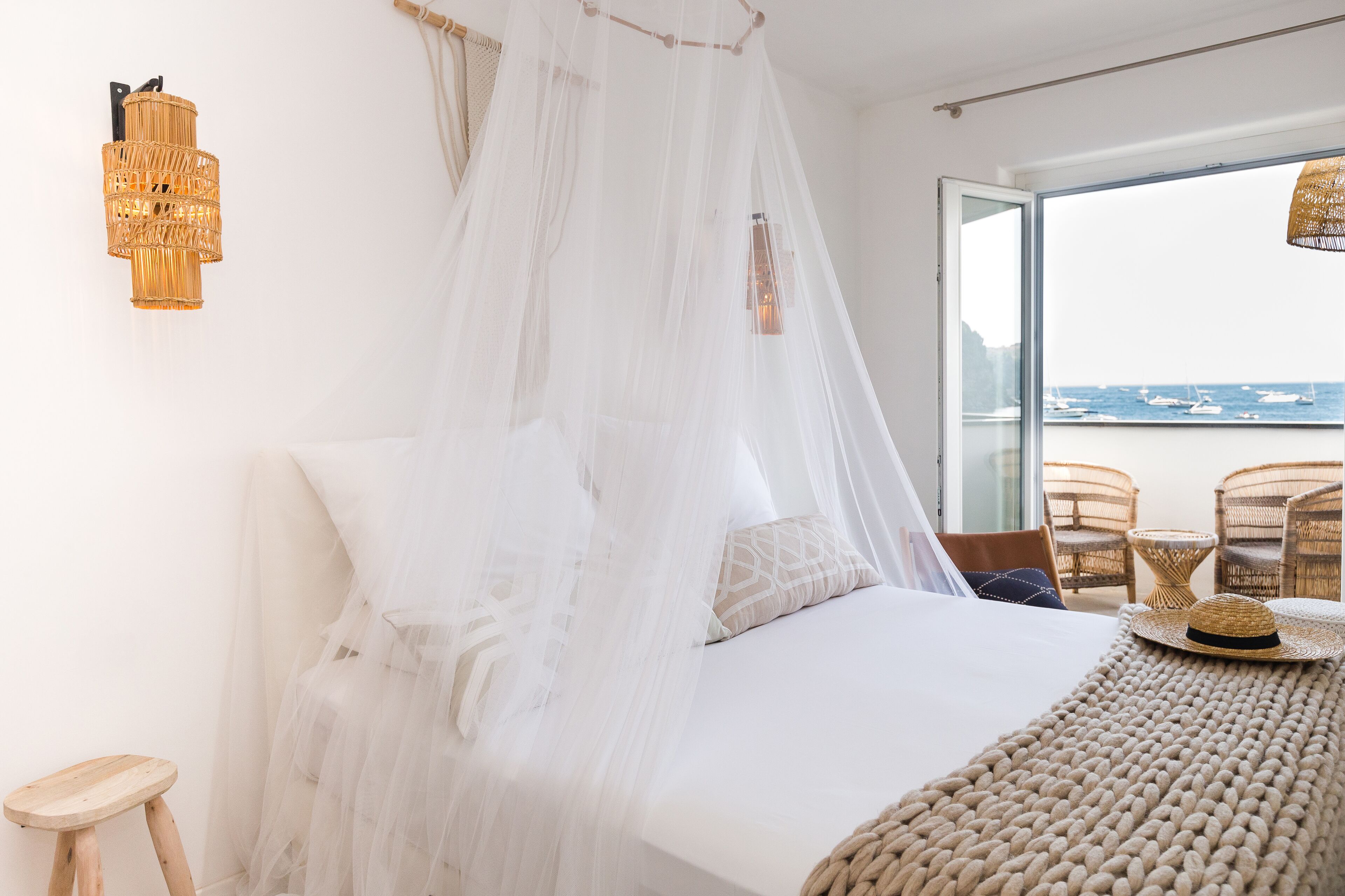 A bedroom with a bed, a canopy, wicker furniture, and a view of the sea.