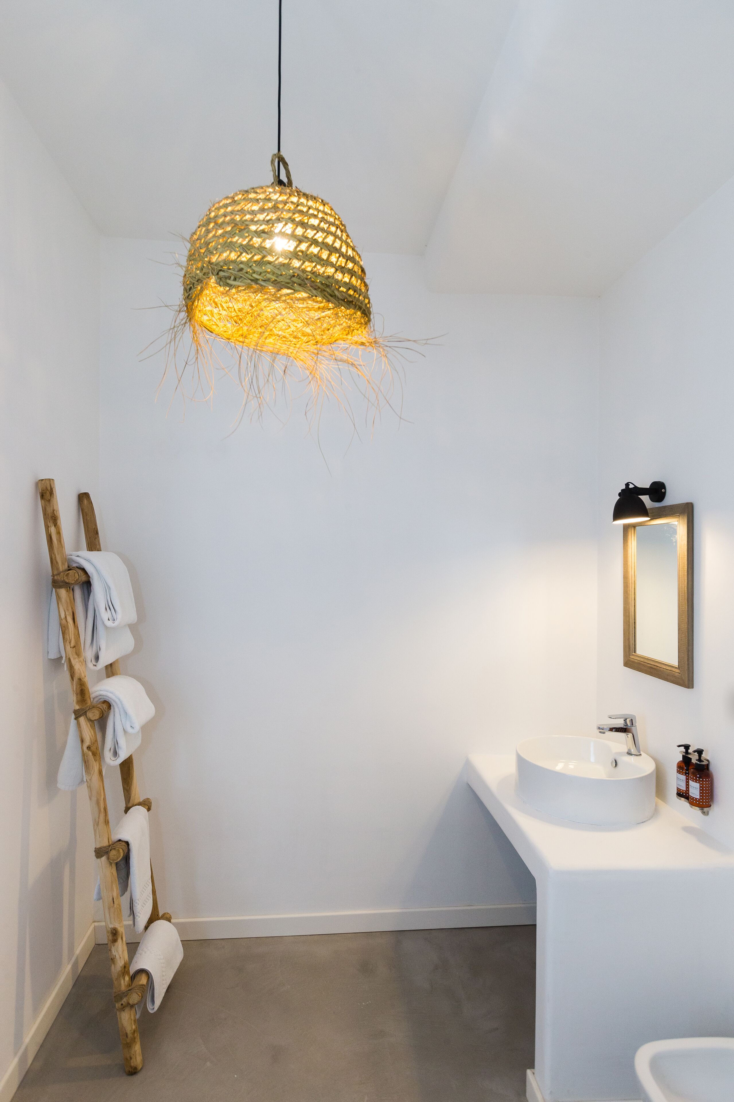 A bathroom with a white sink, a mirror, and a hanging woven light fixture.