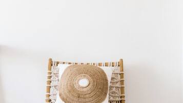 Una silla de madera con respaldo tejido y cojín circular tejido, ubicada frente a una pared blanca con dos adornos de madera en forma de cuerno.