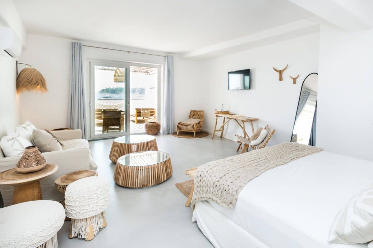 A modern, minimalist bedroom with a large bed, a sofa, a dining table, and a balcony with outdoor seating.
