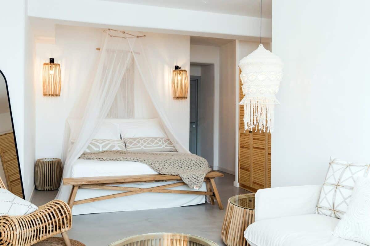 A bedroom with a bed, a canopy, a hanging light fixture, and a white chair.