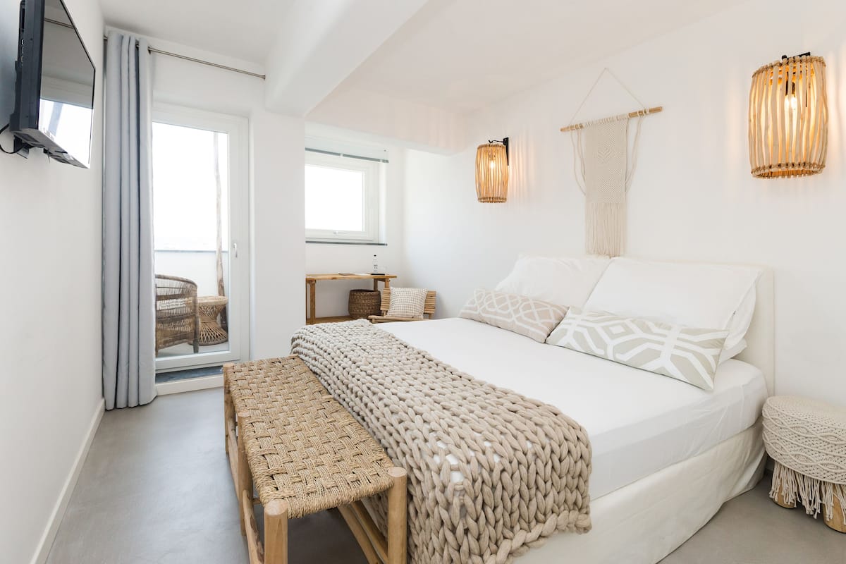 A bedroom with a large bed, a bench, a TV, and a view of the outside.