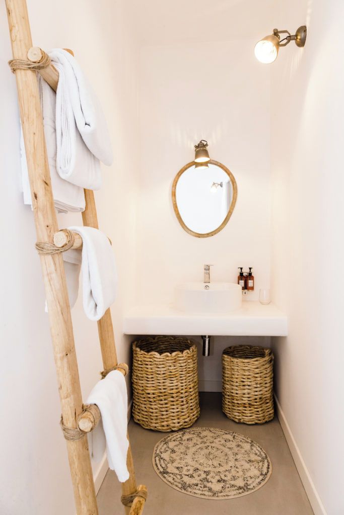 Une salle de bain avec un porte-serviettes en bois, un miroir rond, un lavabo blanc et deux paniers en osier.