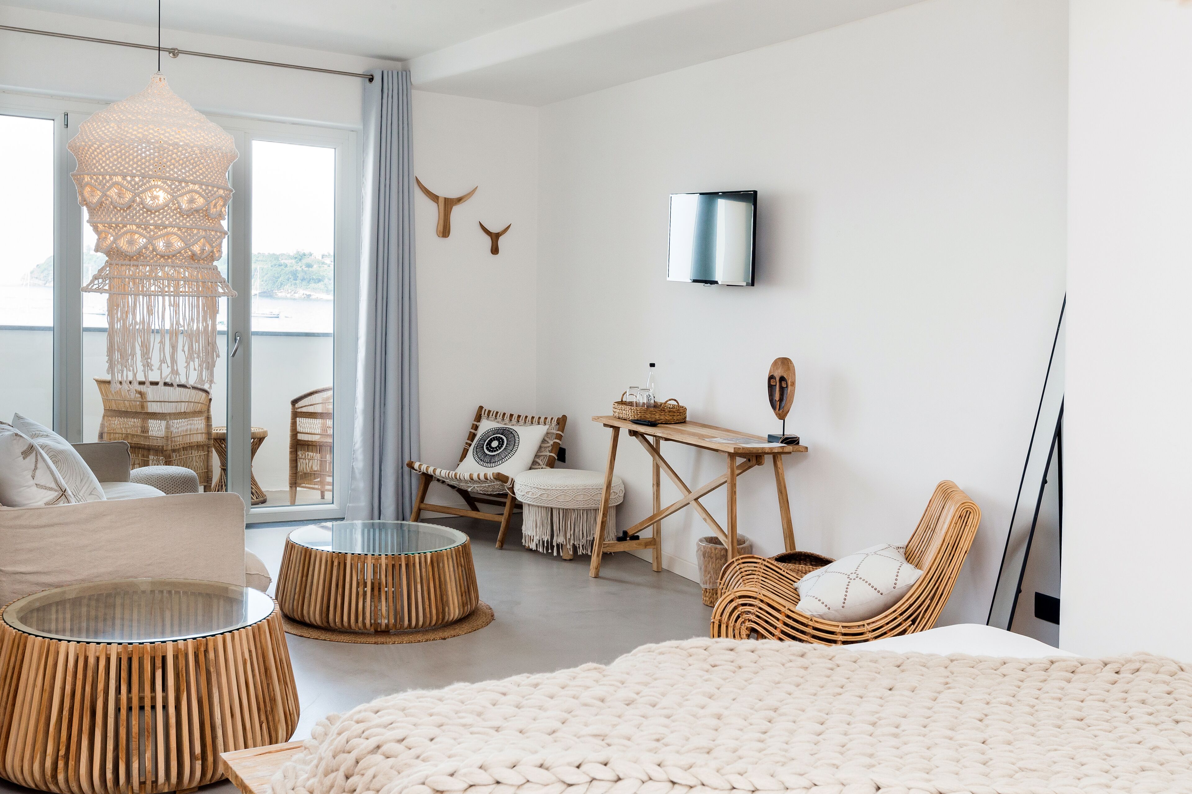 A modern, well-lit room with wicker furniture, a large window, and a mounted flat-screen TV.