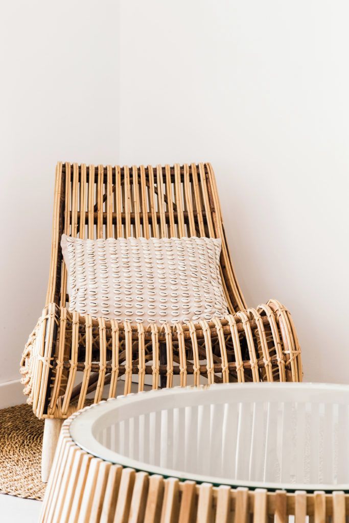 A wicker lounge chair with a textured cushion against a plain wall.