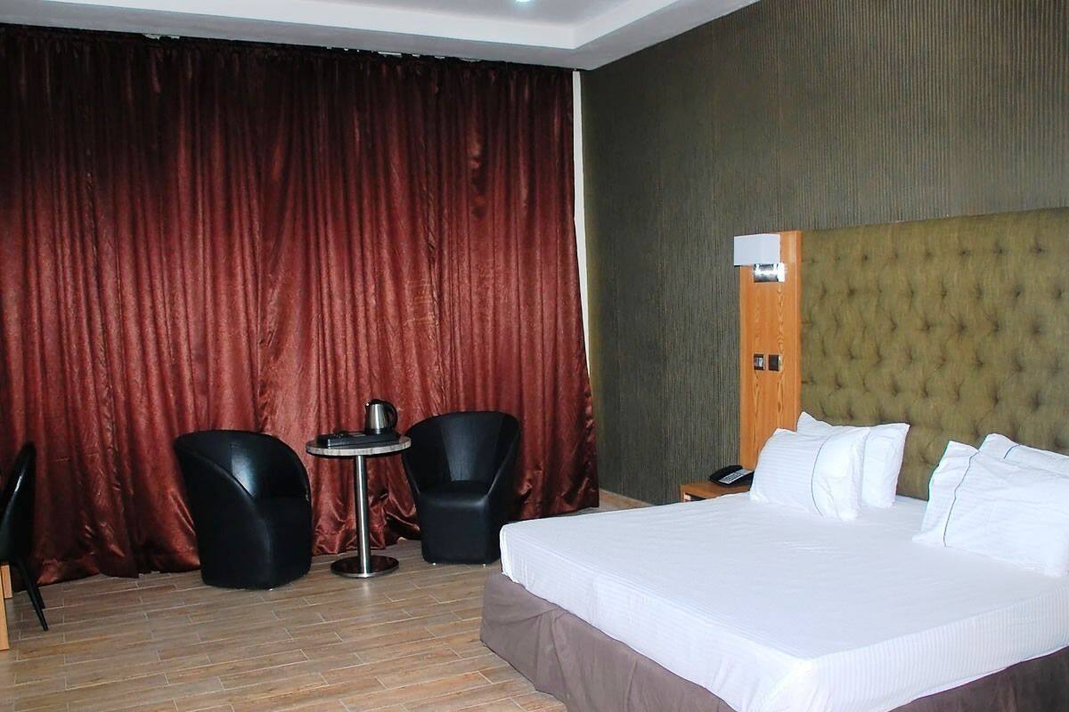 Ein Hotelzimmer mit einem großen Bett, einem runden Tisch, zwei schwarzen Stühlen und einem roten Vorhang.