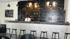 A bar area with a bartender, multiple shelves of bottles, and black chairs with a round table.