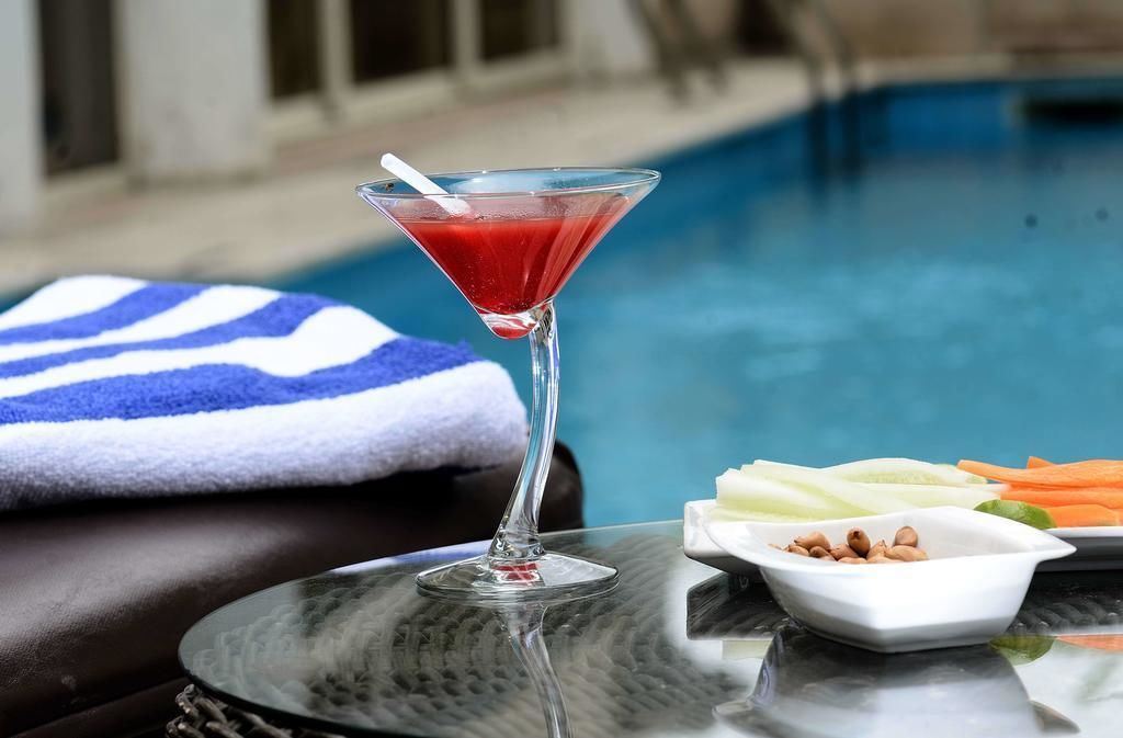 A martini glass with a red drink, a poolside setting, a towel, and a plate with vegetables and nuts.