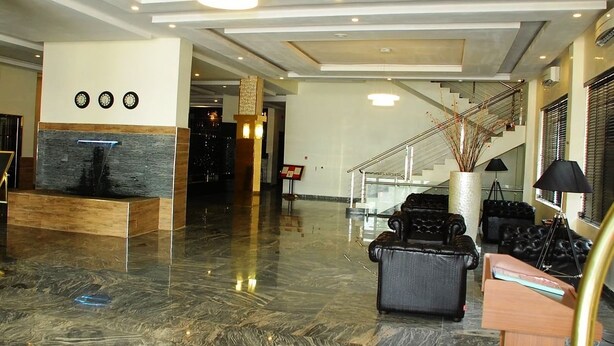 A spacious lobby with a marble floor, a reception desk, a staircase, and a seating area with leather sofas.