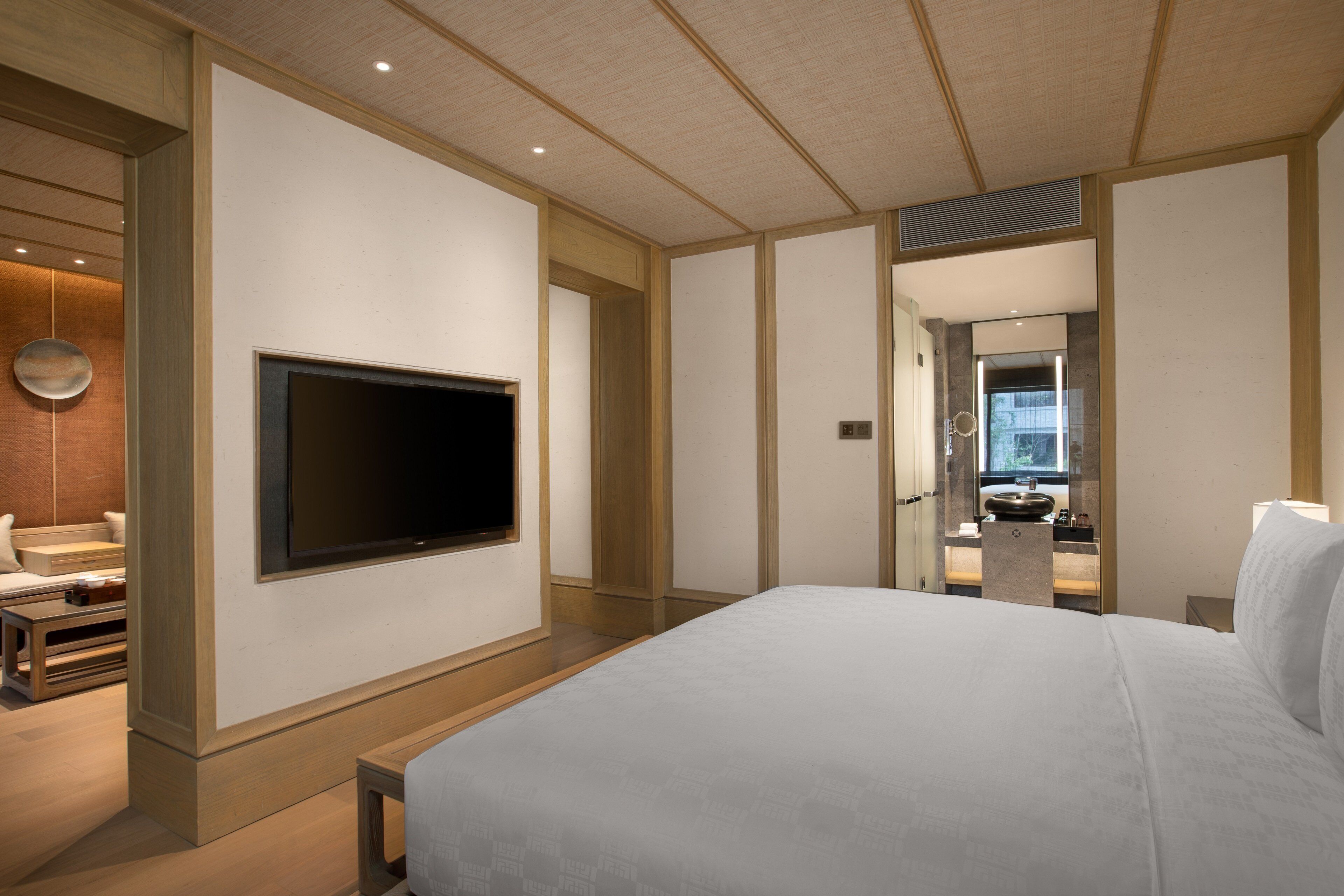Habitación de hotel con una cama grande, un televisor de pantalla plana en la pared, una mesita pequeña y un espejo.