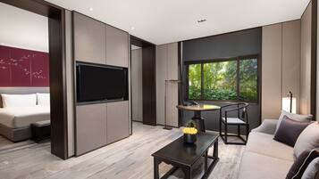 A modern living room with a sofa, a coffee table, a TV, and a window with a view of greenery.