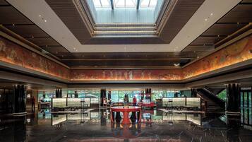 A spacious lobby with a high ceiling, a central seating area, and a large window providing natural light.