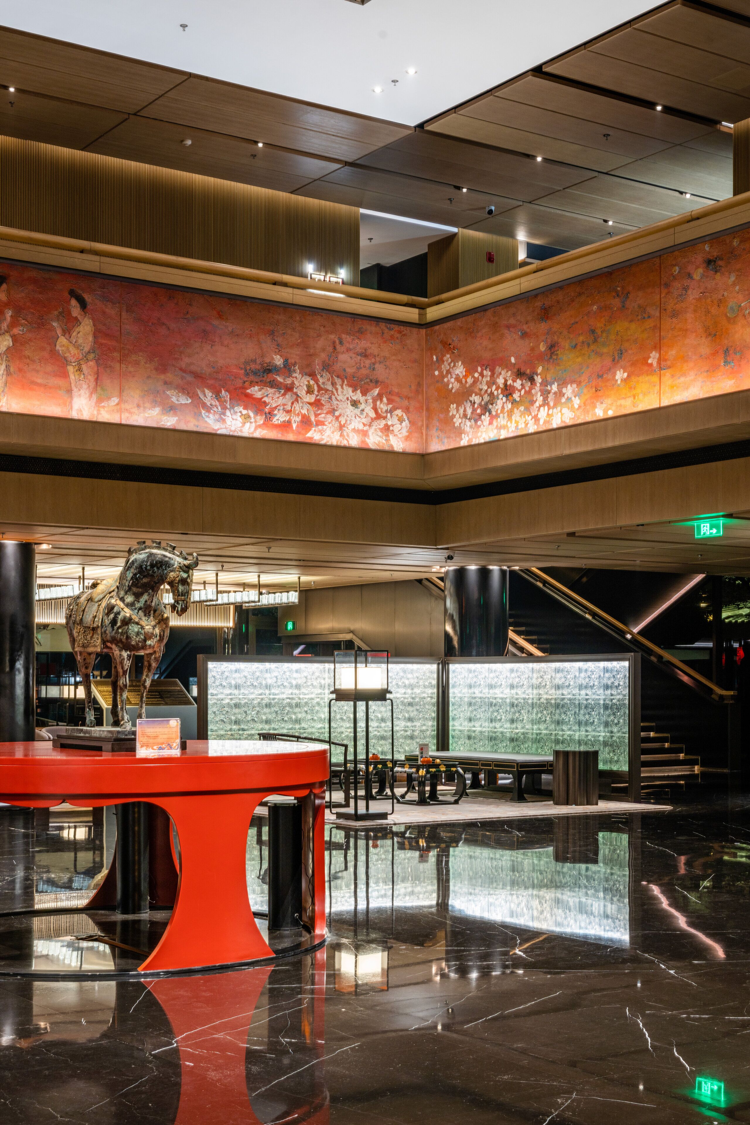A spacious lobby with a large red table, a bronze horse sculpture, and a mural on the wall.