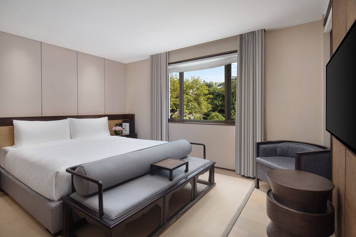 Habitación de hotel moderna con una cama grande, zona de estar, televisión y vistas a zonas verdes.