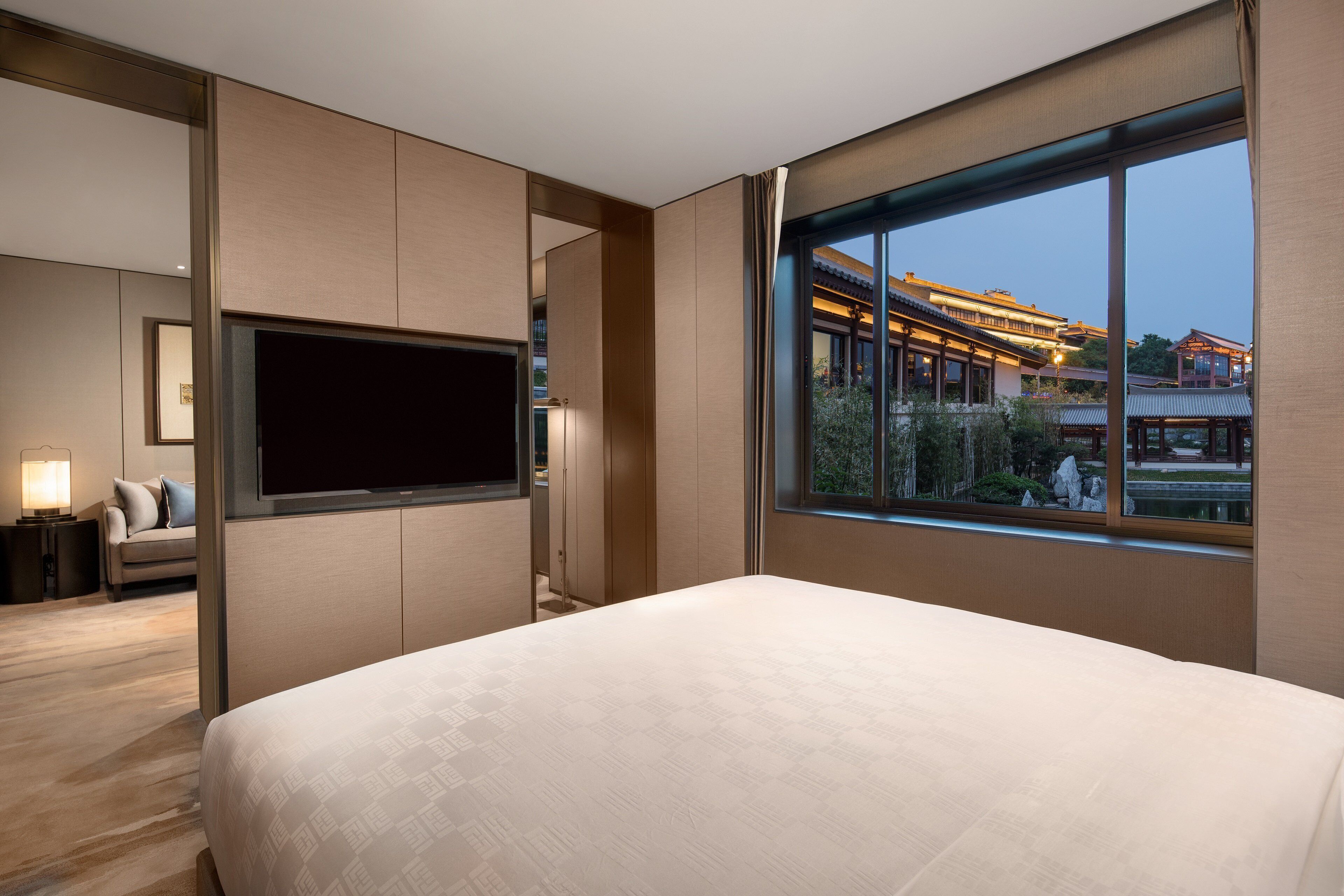 Een moderne hotelkamer met een groot bed, een flatscreen televisie aan de muur en uitzicht op traditionele architectuur door een groot raam.