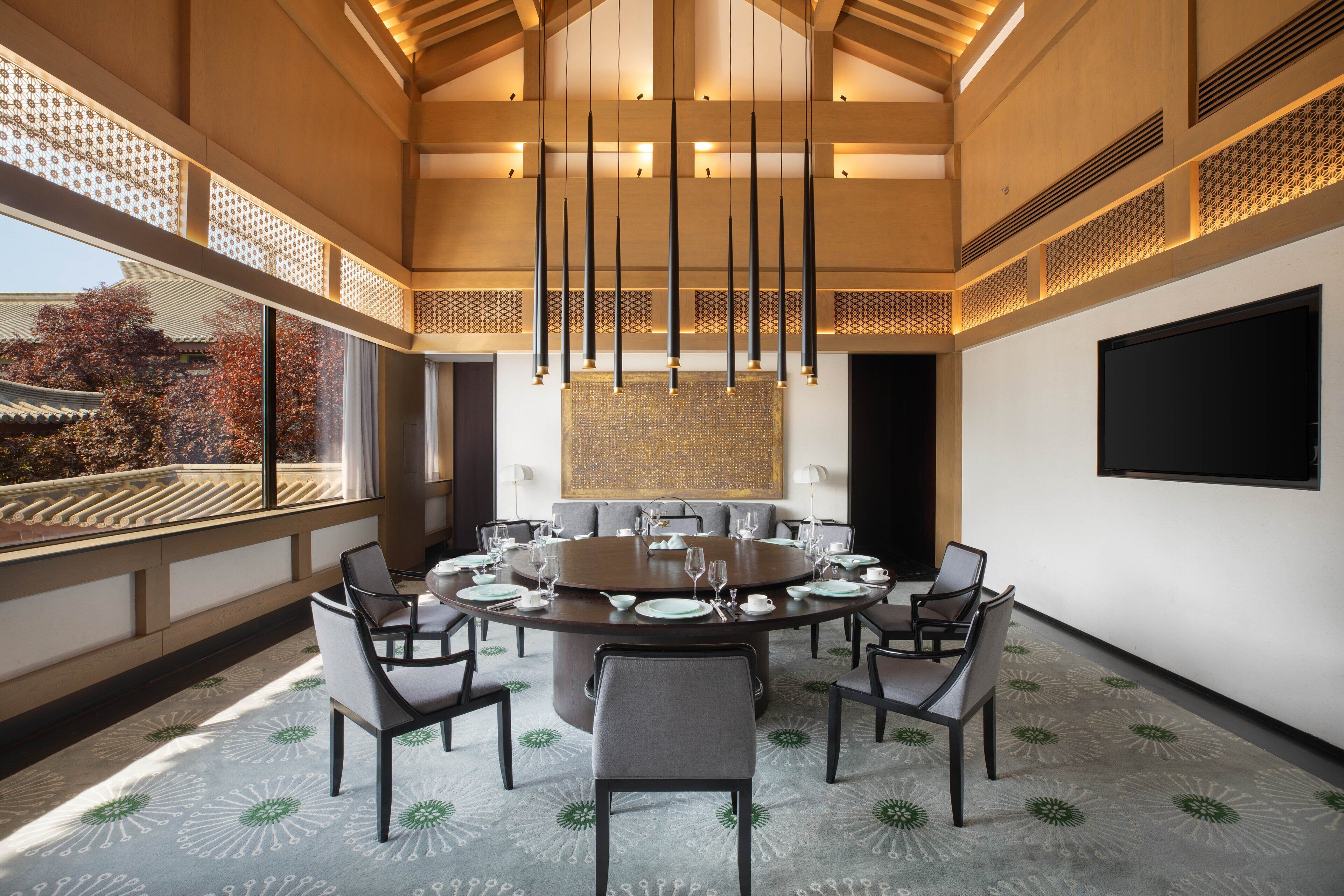 A modern dining room with a round table, chairs, and a large window overlooking a traditional building.