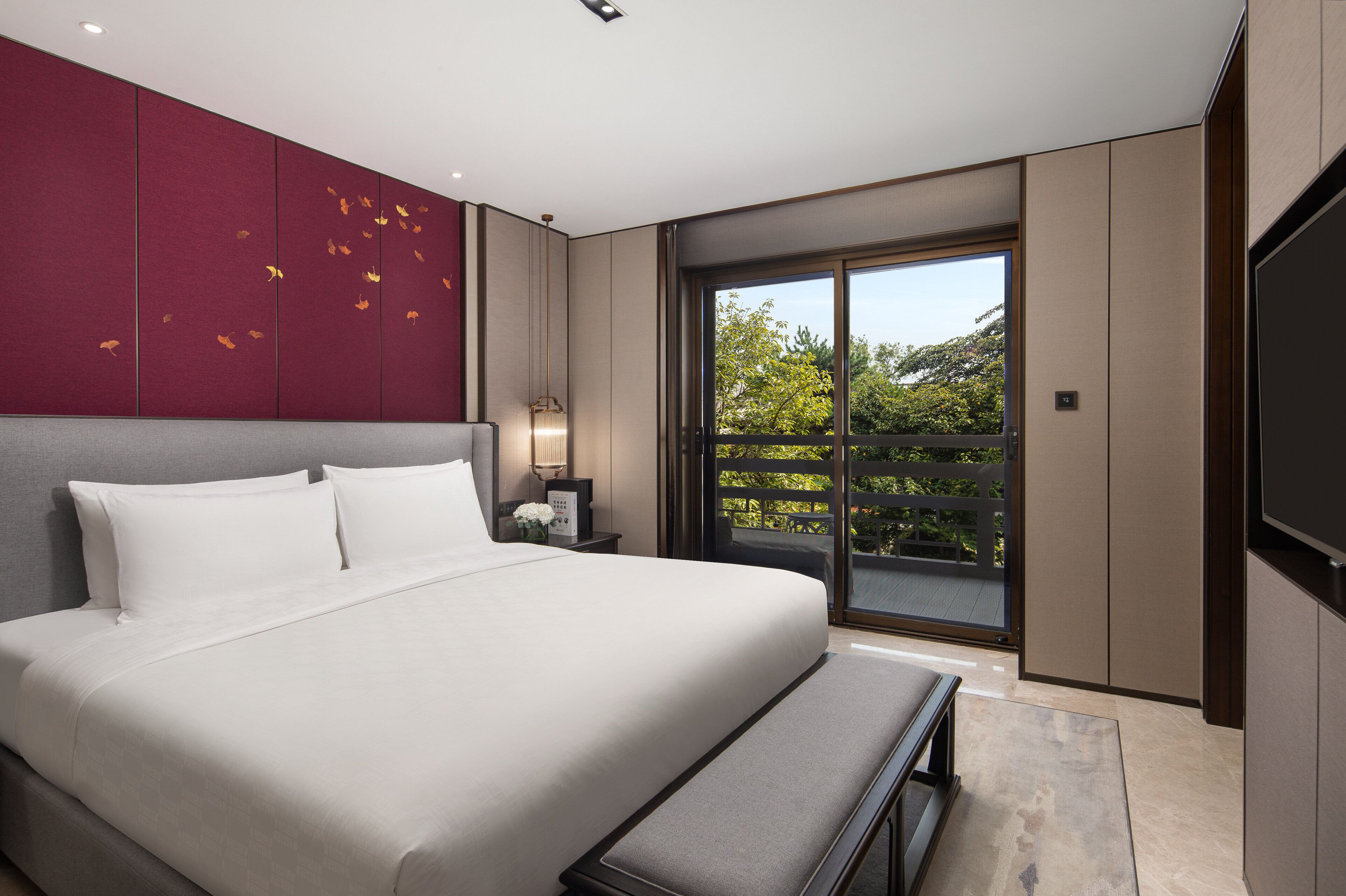 A modern bedroom with a large bed, a bench, a nightstand, and a sliding glass door to a balcony.